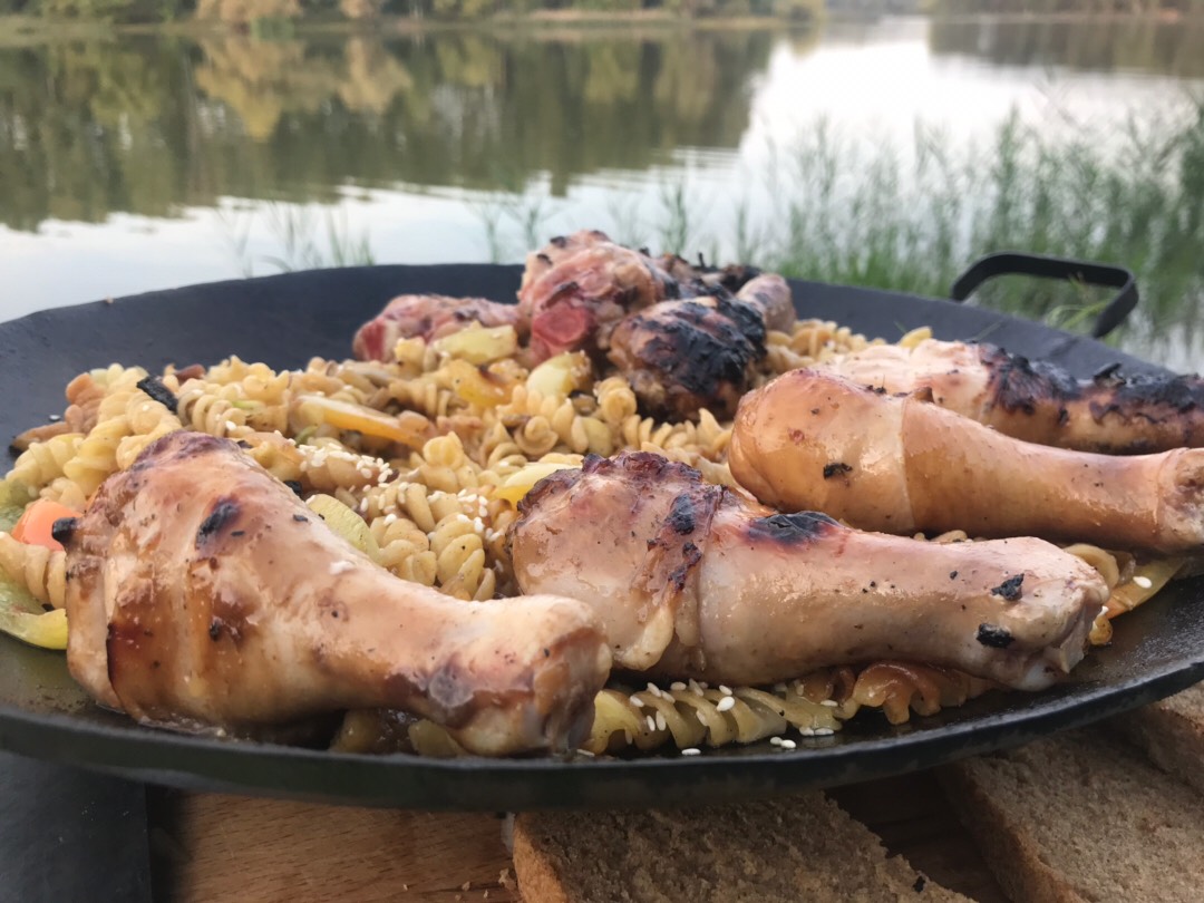 Жареные макароны с овощами и куриными ножками на костре на берегу озера